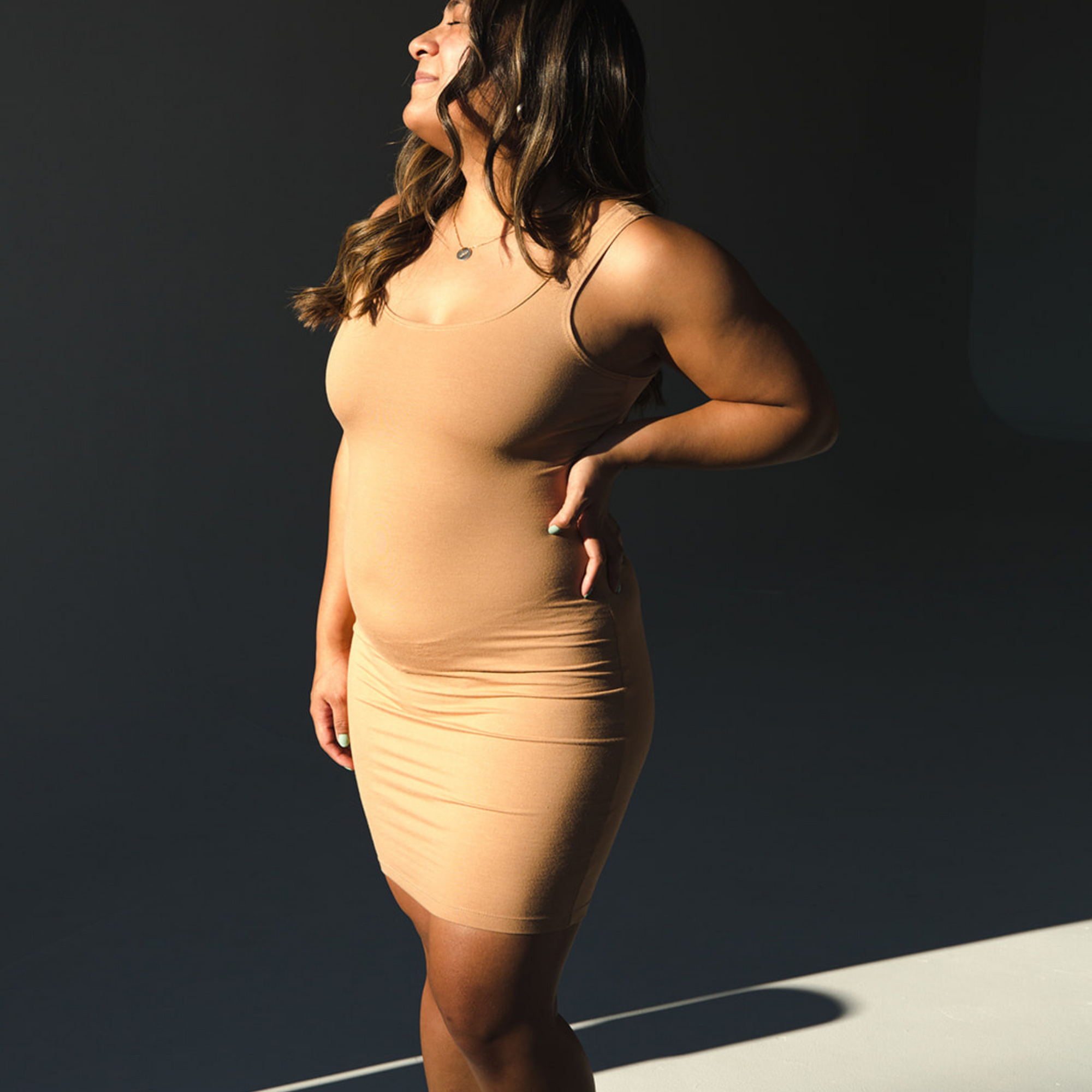 Product shot of NŪD Apparel Tayler Slip Dress, wide strap, fitted style and seamless, made of bamboo fabric produced in California, in Medium Nude on medium-skinned model, frontt/side shot