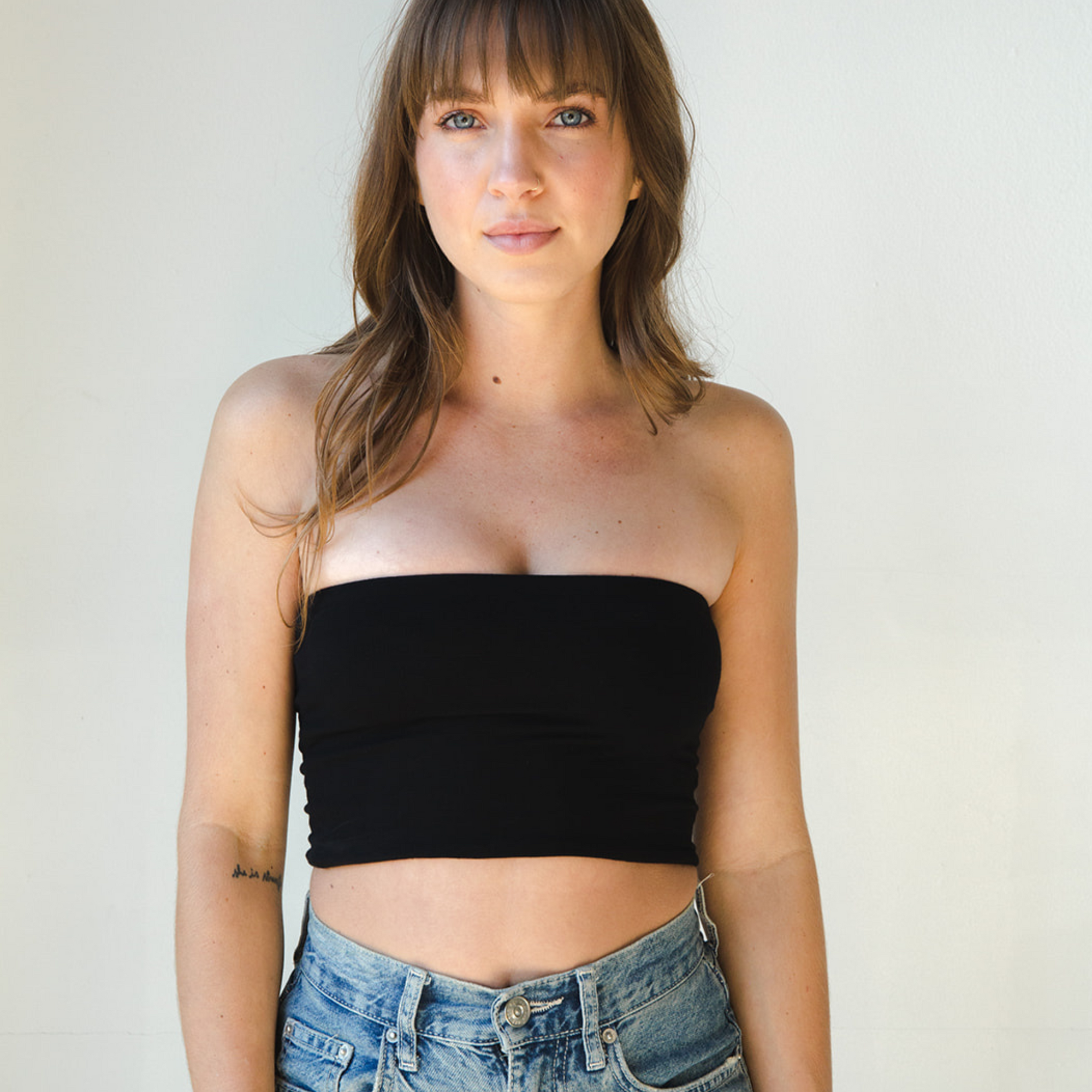 Product shot of NŪD Apparel Hunter Double-Layered Bandeau, strapless, cropped and seamless style, made of bamboo fabric produced in California, in Black on fair-skinned model paired with medium-wash jeans, front shot