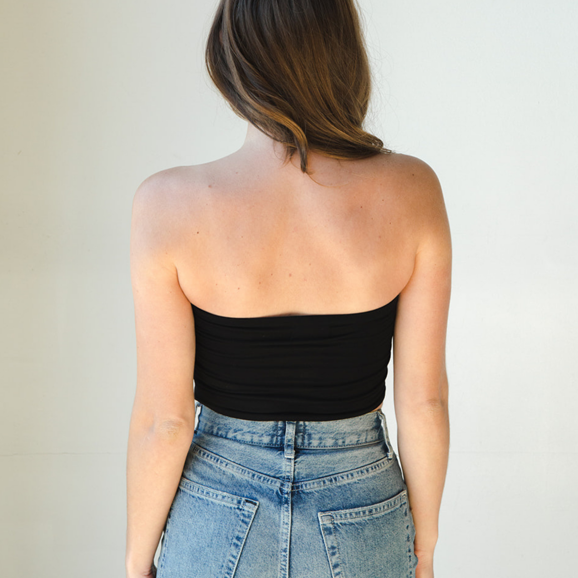 Product shot of NŪD Apparel Hunter Double-Layered Bandeau, strapless, cropped and seamless style, made of bamboo fabric produced in California, in Black on fair-skinned model paired with medium-wash jeans, back shot