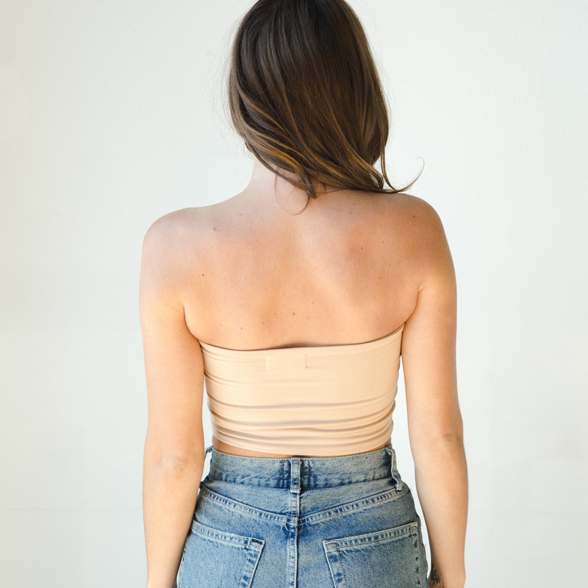 Product shot of NŪD Apparel Hunter Double-Layered Bandeau, strapless, cropped and seamless style, made of bamboo fabric produced in California, in Light Nude on fair-skinned model paired with medium-wash jeans, back shot