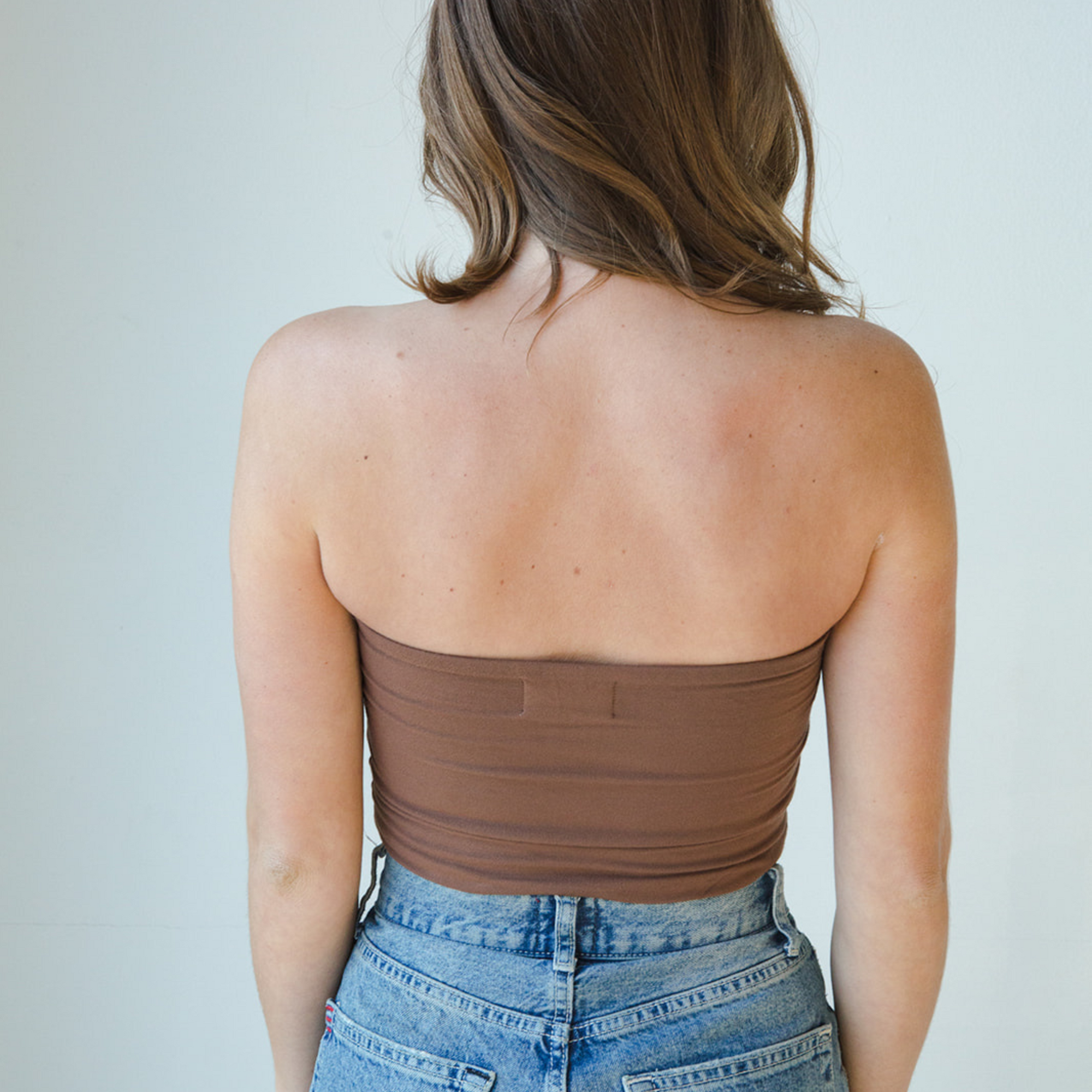 Product shot of NŪD Apparel Hunter Double-Layered Bandeau, strapless, cropped and seamless style, made of bamboo fabric produced in California, in Dark Nude on fair-skinned model paired with medium-wash jeans, back shot