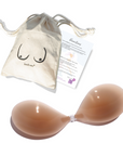 Product shot of reusable and sticky Medium Tint Silicone Stick-on Bra with a branded drawstring unbleached cotton muslin pouch packaging and information insert card with wear and care instructions, showing thin edge of the Silicone Stick-on Bra
