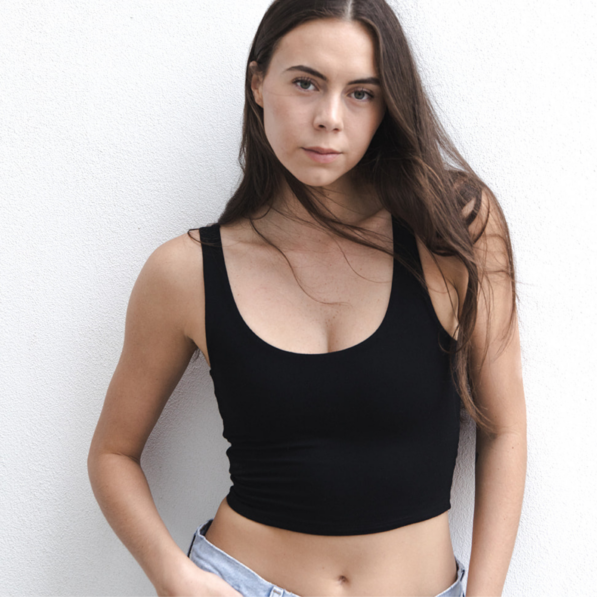 Product shot of NŪD Apparel Devon Double Layered Scoop Crop top, wide strap and seamless, made of bamboo fabric produced in California, in Black on fair-skinned model paired with light-wash jeans, front close-up shot