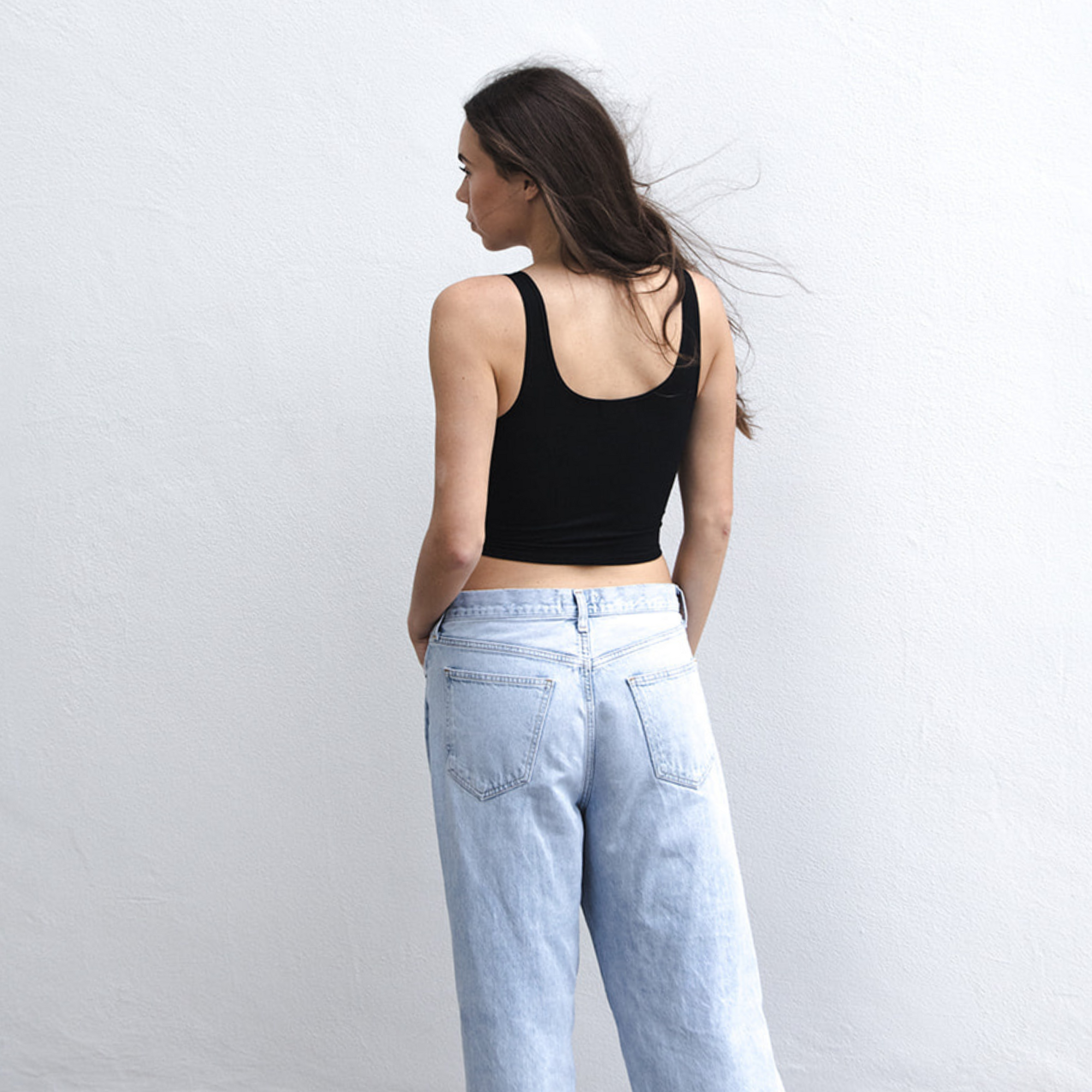 Product shot of NŪD Apparel Devon Double Layered Scoop Crop top, wide strap and seamless, made of bamboo fabric produced in California, in Black on fair-skinned model paired with light-wash jeans, back shot