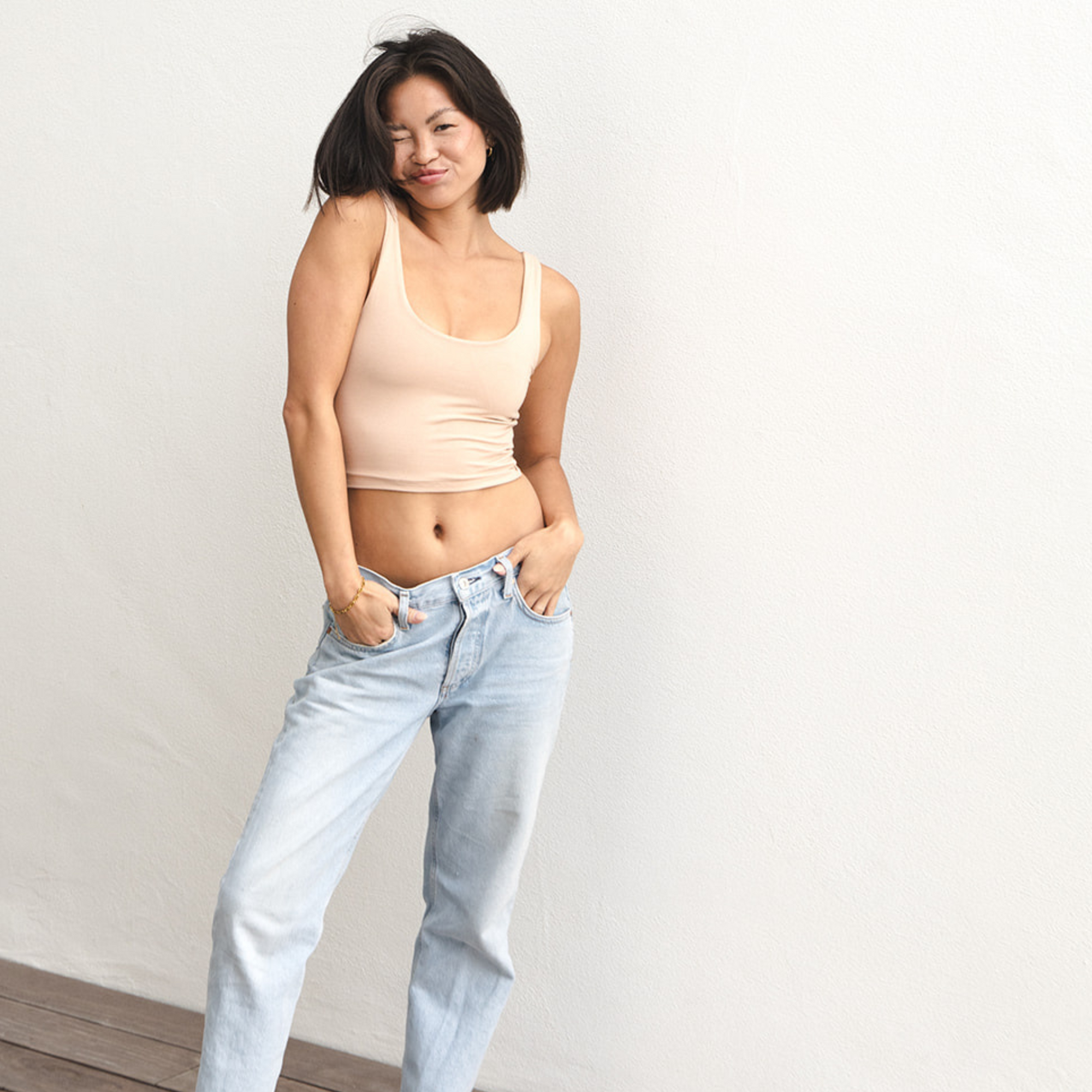 Product shot of NŪD Apparel Devon Double Layered Scoop Crop top, wide strap and seamless, made of bamboo fabric produced in California, in Light Nude on fair-skinned model paired with light-wash jeans, front wide shot