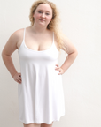 Product shot of NŪD Apparel Betty Swinging Slip Dress, thin adjustable strap, loose style and with shelf bra, made of bamboo fabric produced in California, in White on fair-skinned model, front shot