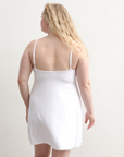Product shot of NŪD Apparel Betty Swinging Slip Dress, thin adjustable strap, loose style and with shelf bra, made of bamboo fabric produced in California, in White on fair-skinned model, back shot