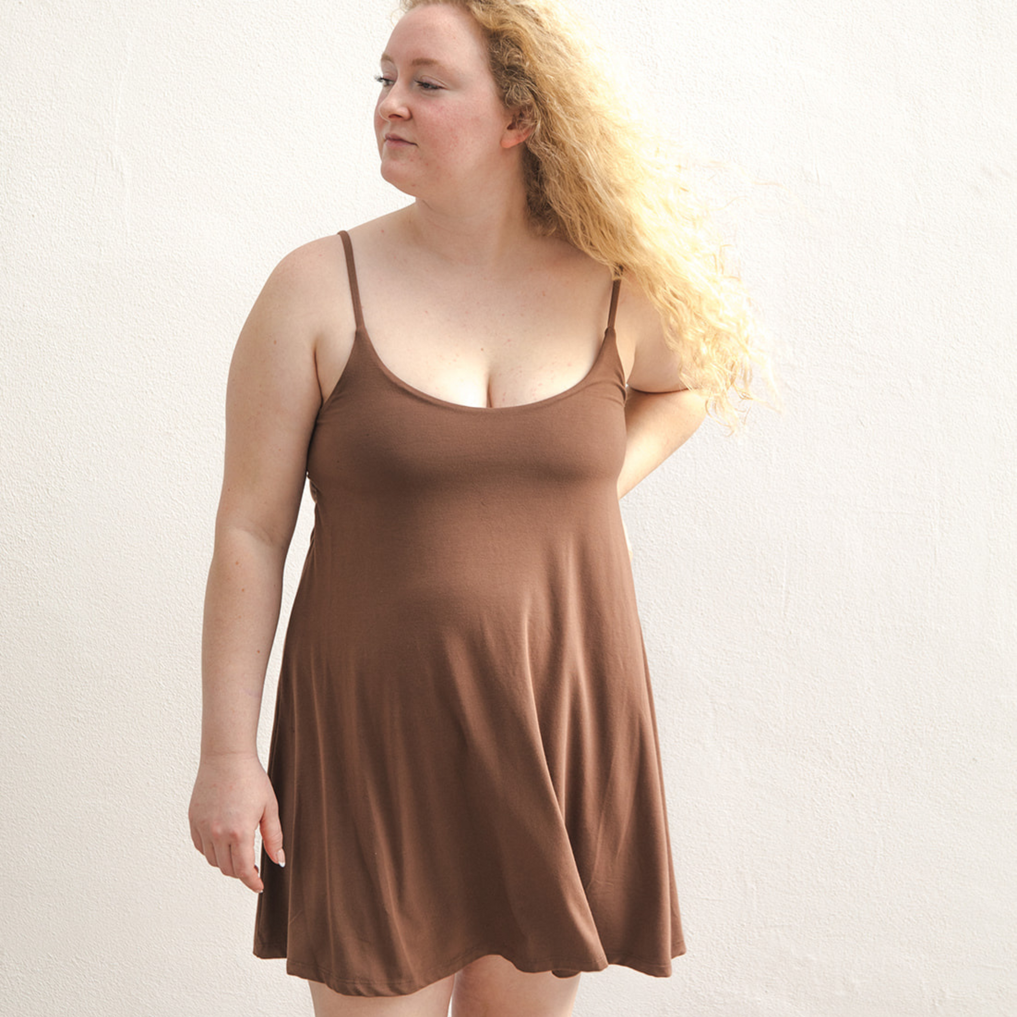 Product shot of NŪD Apparel Betty Swinging Slip Dress, thin adjustable strap, loose style and with shelf bra, made of bamboo fabric produced in California, in Dark Nude on fair-skinned model, front shot