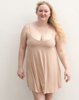 Product shot of NŪD Apparel Betty Swinging Slip Dress, thin adjustable strap, loose style and with shelf bra, made of bamboo fabric produced in California, in Light Nude on fair-skinned model, front shot