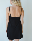 Product shot of NŪD Apparel Betty Swinging Slip Dress, thin adjustable strap, loose style and with shelf bra, made of bamboo fabric produced in California, in Black on fair-skinned model, back shot