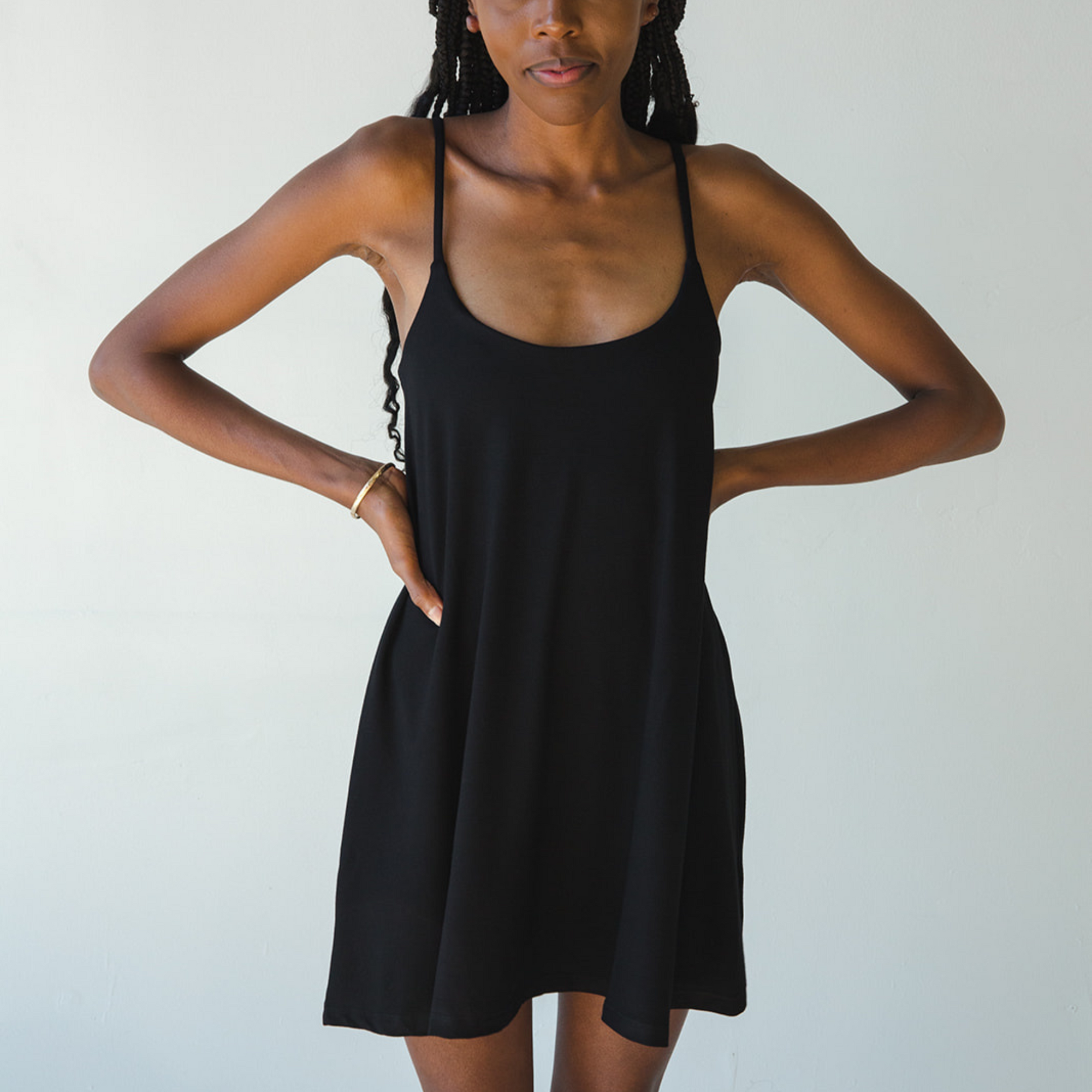 Product shot of NŪD Apparel Betty Swinging Slip Dress, thin adjustable strap, loose style and with shelf bra, made of bamboo fabric produced in California, in Black on dark-skinned model, front shot