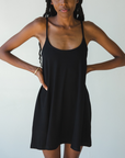 Product shot of NŪD Apparel Betty Swinging Slip Dress, thin adjustable strap, loose style and with shelf bra, made of bamboo fabric produced in California, in Black on dark-skinned model, front shot