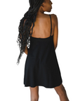 Product shot of NŪD Apparel Betty Swinging Slip Dress, thin adjustable strap, loose style and with shelf bra, made of bamboo fabric produced in California, in Black on dark-skinned model, back shot