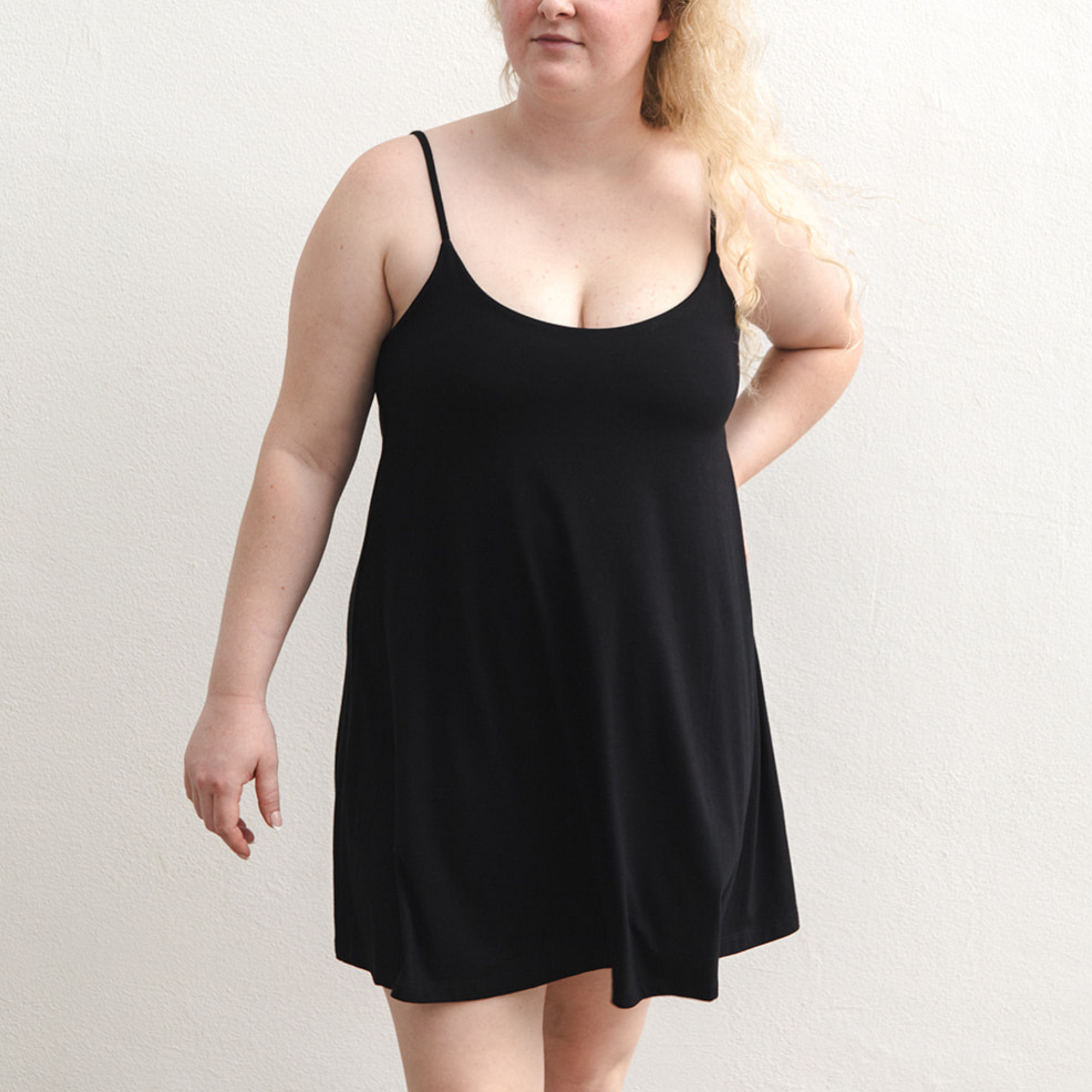 Product shot of NŪD Apparel Betty Swinging Slip Dress, thin adjustable strap, loose style and with shelf bra, made of bamboo fabric produced in California, in Black on fair-skinned model, front shot
