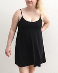 Product shot of NŪD Apparel Betty Swinging Slip Dress, thin adjustable strap, loose style and with shelf bra, made of bamboo fabric produced in California, in Black on fair-skinned model, front shot