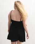 Product shot of NŪD Apparel Betty Swinging Slip Dress, thin adjustable strap, loose style and with shelf bra, made of bamboo fabric produced in California, in Black on fair-skinned model, back shot