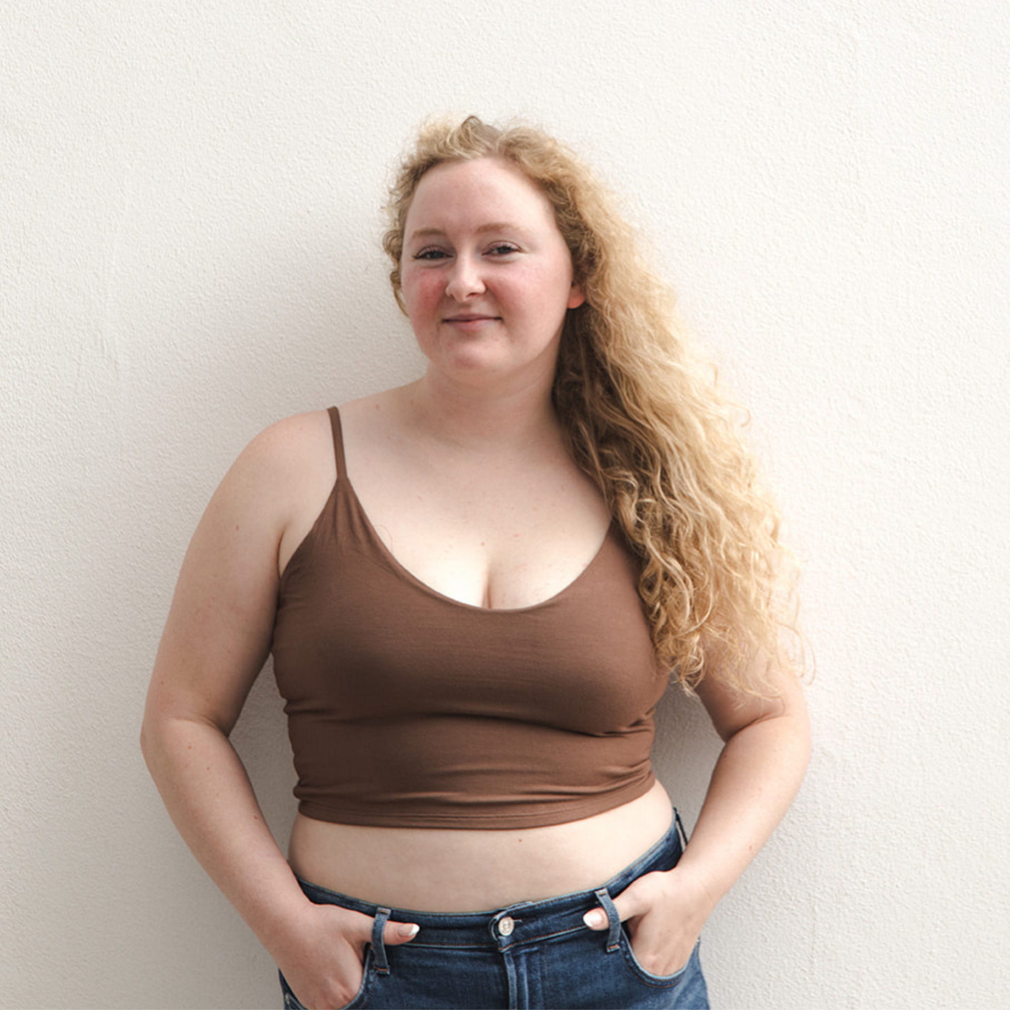 Product shot of NŪD Apparel Kyla Double Layered Crop top, thin strap and seamless, made of bamboo fabric produced in California, in Dark Nude on fair-skinned model paired with dark-wash jeans, front shot
