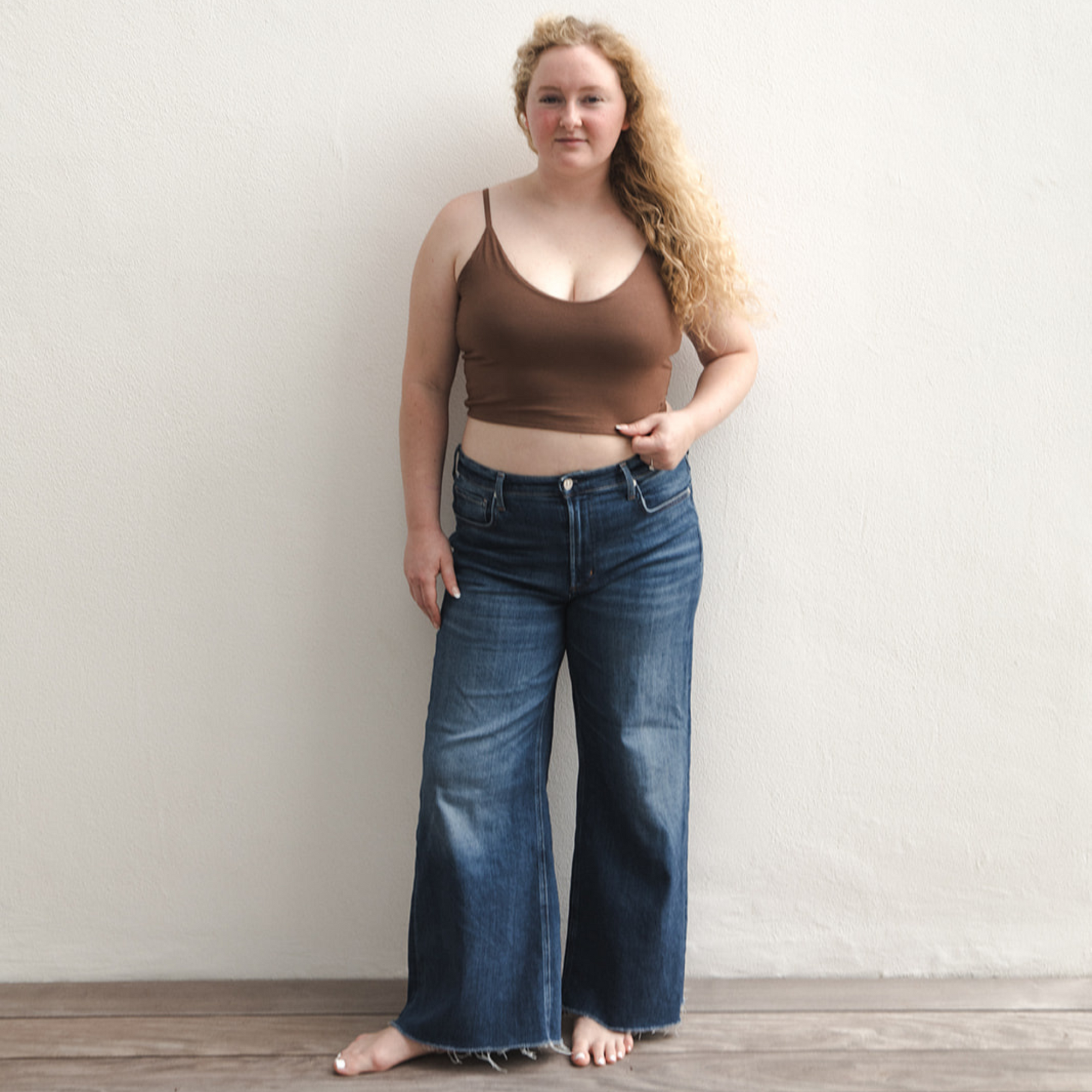 Product shot of NŪD Apparel Kyla Double Layered Crop top, thin strap and seamless, made of bamboo fabric produced in California, in Dark Nude on fair-skinned model paired with dark-wash jeans, front wide shot