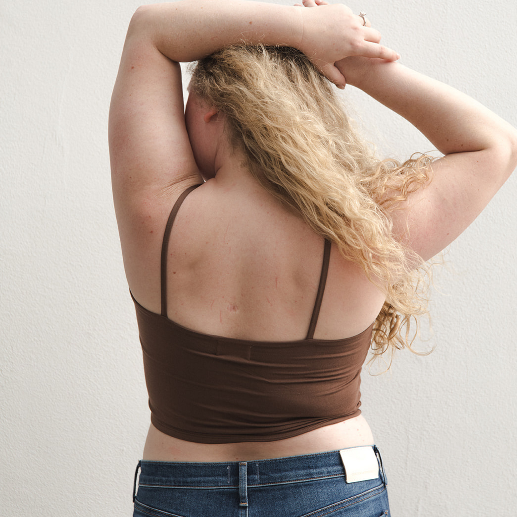 Product shot of NŪD Apparel Kyla Double Layered Crop top, thin strap and seamless, made of bamboo fabric produced in California, in Dark Nude on fair-skinned model paired with dark-wash jeans, back shot
