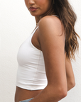 Product shot of NŪD Apparel Kyla Double Layered Crop top, thin strap and seamless, made of bamboo fabric produced in California, in White on medium-skinned model paired with light-wash jeans, front/side shot