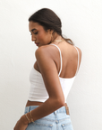 Product shot of NŪD Apparel Kyla Double Layered Crop top, thin strap and seamless, made of bamboo fabric produced in California, in White on medium-skinned model paired with light-wash jeans, back/side shot