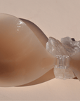 Product shot of a reusable Medium tint Silicone Stick-on Bra laying against silica crystal on a light pink background, close-up shot of clasp and thin edge of the Silicone Stick-on Bra