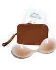 Product shot of sticky Light tint Silicone Stick-on Bra and durable Silicone Travel Case for Silicone Stick-on Bras in Dark Nude and information insert card with wear and care instructions, against a white background showing the thin edges of the Silicone Stick-on Bra
