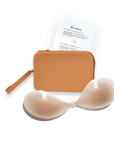 Product shot of sticky Light tint Silicone Stick-on Bra and durable Silicone Travel Case for Silicone Stick-on Bras in Medium Nude and information insert card with wear and care instructions, against a white background showing the thin edges of the Silicone Stick-on Bra