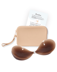 Product shot of sticky Dark tint Silicone Stick-on Bra and durable Silicone Travel Case for Silicone Stick-on Bras in Light Nude and information insert card with wear and care instructions, against a white background showing the thin edges of the Silicone Stick-on Bra