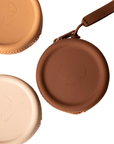 Product shot of our reusable Silicone Travel Cases for Headlight Hiders in Light Nude, Medium Nude and Dark Nude, with Headlight Hiders laying underneath the Silicone Travel Cases, against a white background