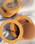 Product shot of a Boob-eez Bamboo Compact with Dark tint Headlight Hiders inside with Bamboo Compacts and nipple covers in the background, close-up shot showing the beautiful wood grain of the bamboo and the magnetic closure