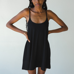Product shot of NŪD Apparel Betty Swinging Slip Dress, thin adjustable strap, loose style and with shelf bra, made of bamboo fabric produced in California, in Black on dark-skinned model, front shot