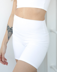 Product shot NŪD Apparel Zoë Biker Short, perfect length, no front seam and comfy, made of bamboo fabric produced in California, in White on a fair-skinned model, paired with Hunter Bandeau, front/side shot