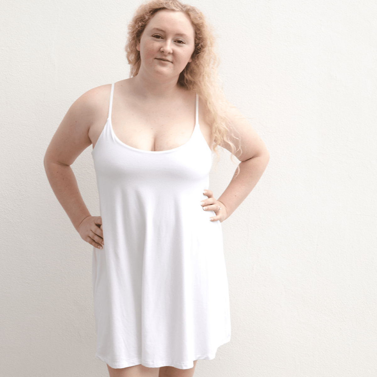 Product shot of NŪD Apparel Betty Swinging Slip Dress, thin adjustable strap, loose style and with shelf bra, made of bamboo fabric produced in California, in White on fair-skinned model, front shot