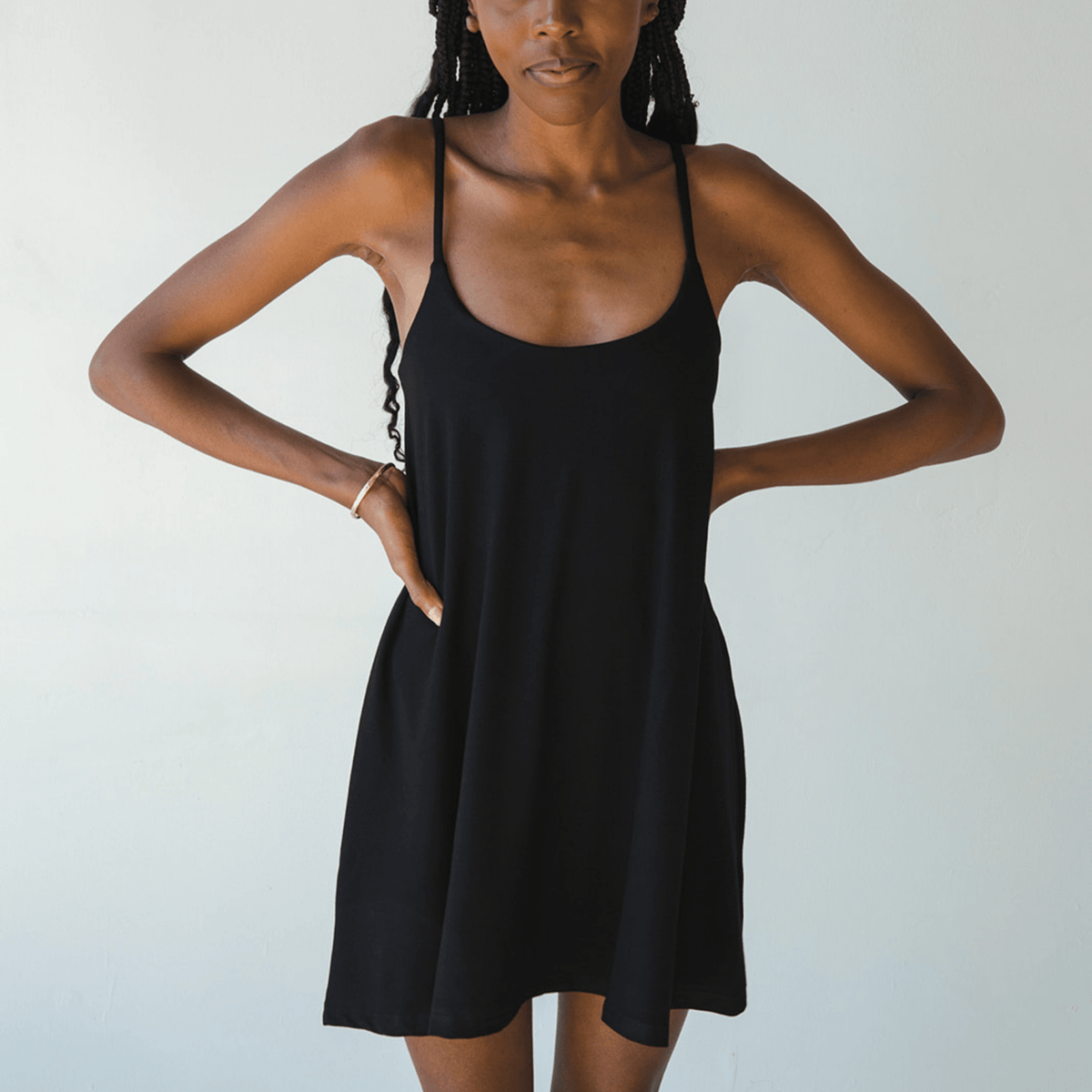 Product shot of NŪD Apparel Betty Swinging Slip Dress, thin adjustable strap, loose style and with shelf bra, made of bamboo fabric produced in California, in Black on dark-skinned model, front shot