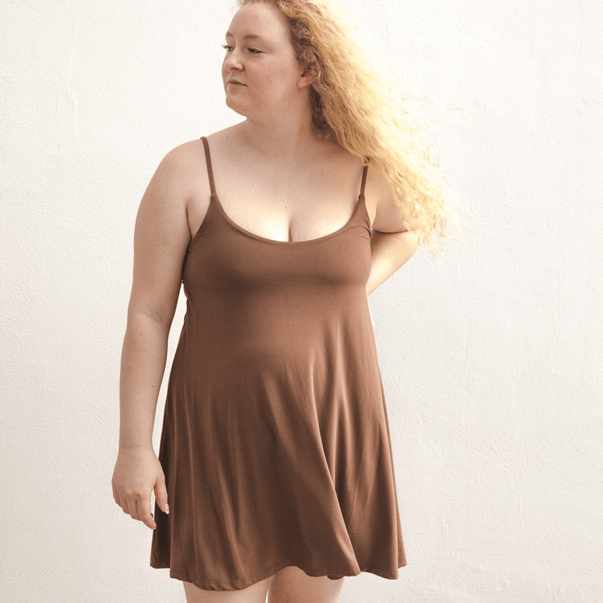 Product shot of NŪD Apparel Betty Swinging Slip Dress, thin adjustable strap, loose style and with shelf bra, made of bamboo fabric produced in California, in Dark Nude on fair-skinned model, front shot