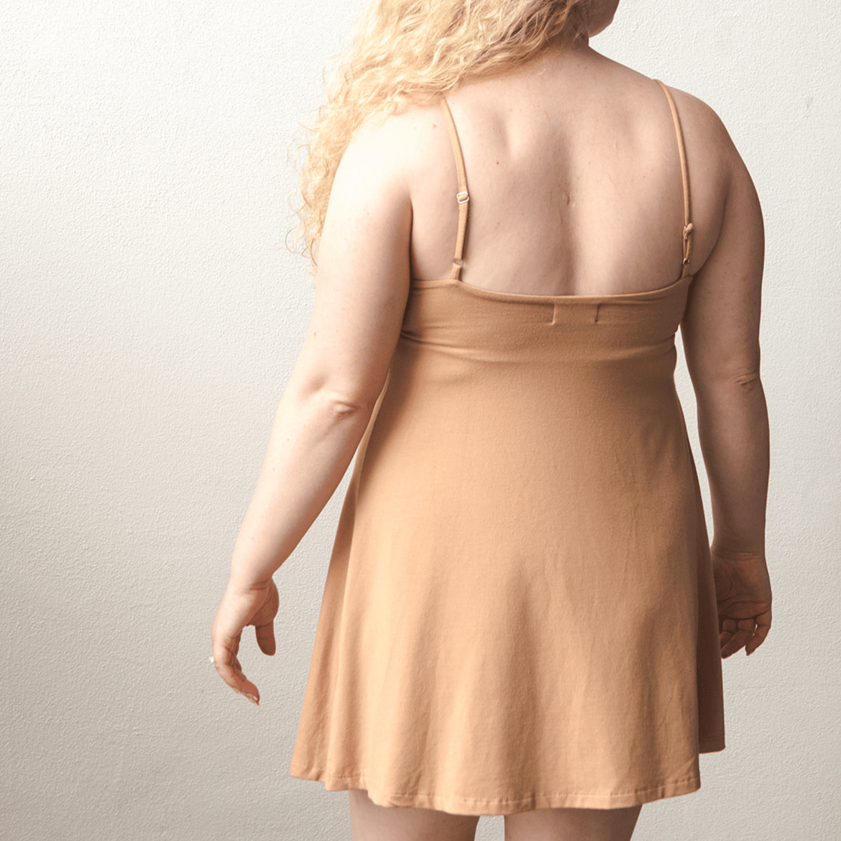 Product shot of NŪD Apparel Betty Swinging Slip Dress, thin adjustable strap, loose style and with shelf bra, made of bamboo fabric produced in California, in Medium Nude on fair-skinned model, back shot