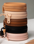 Product shot of a stack of reusable Silicone Travel Cases for Headlight Hiders in Medium Nude, Light Nude, Dark Nude, Dusty Pink, and Black, showing the zipper detail and removable strap
