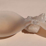 Product shot of reusable and sticky Light tint Silicone Stick-on Bra laying against silica crystal and light pink background, close-up shot showing the clasp and razor thin edges of the Silicone Stick-on Bra