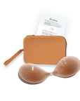 Product shot of sticky Medium tint Silicone Stick-on Bra and durable Silicone Travel Case for Silicone Stick-on Bra in Medium Nude and an information insert card with wear and care instructions, against a white background showing the razor thin edges of the Silicone Stick-on Bra