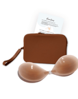 Product shot of sticky Medium tint Silicone Stick-on Bra and durable Silicone Travel Case for Silicone Stick-on Bras in Dark Nude and information insert card with wear and care instructions, against a white background showing the thin edges of the Silicone Stick-on Bra