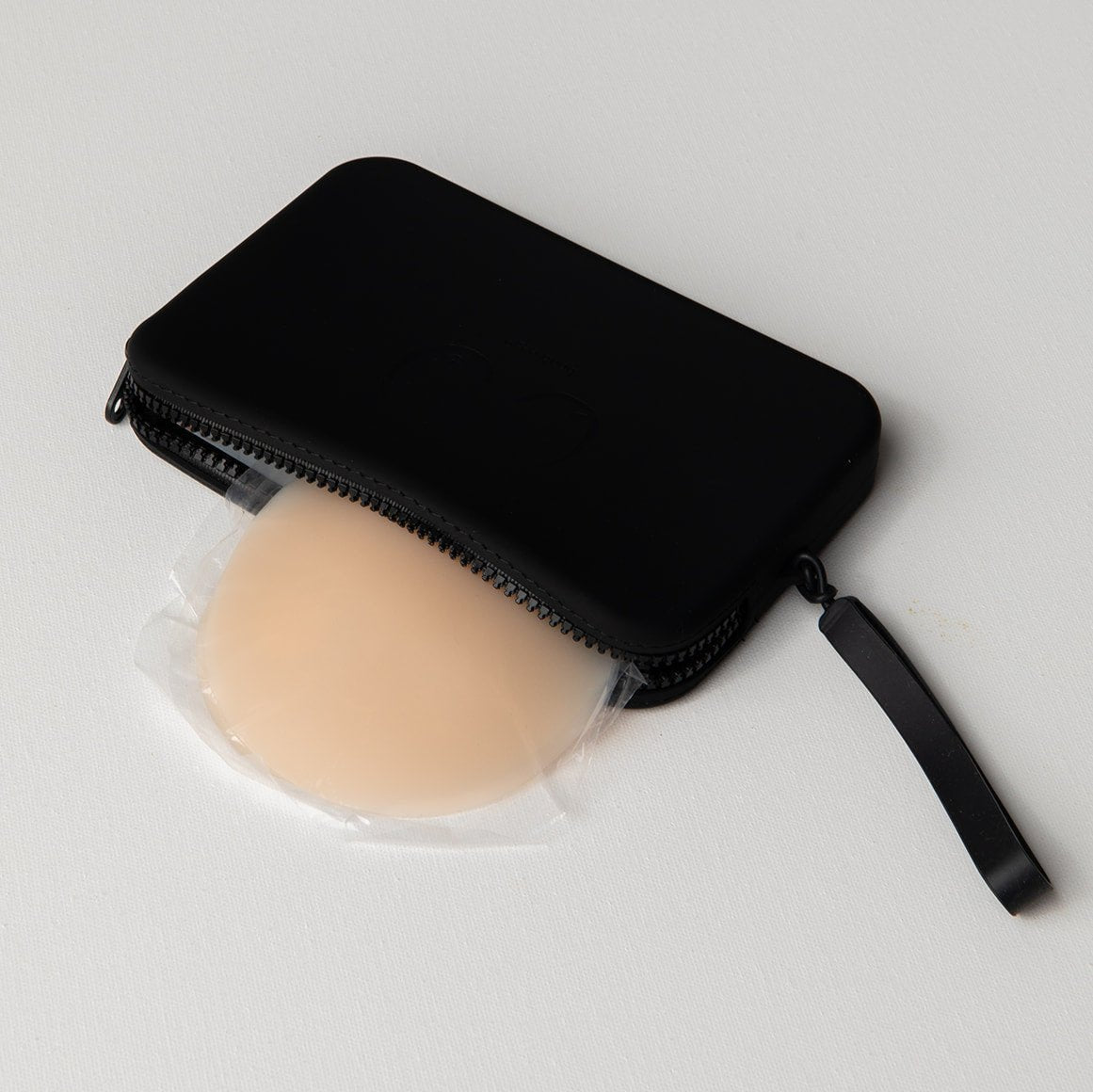 Product shot of our sticky Silicone Stick-on Bra in Light tint and our durable Silicone Travel Case in Black, showing the removable strap and zipper closure 
