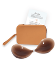 Product shot of sticky Dark tint Silicone Stick-on Bra and durable Silicone Travel Case for Silicone Stick-on Bras in Medium Nude and information insert card with wear and care instructions, against a white background showing the thin edges of the Silicone Stick-on Bra
