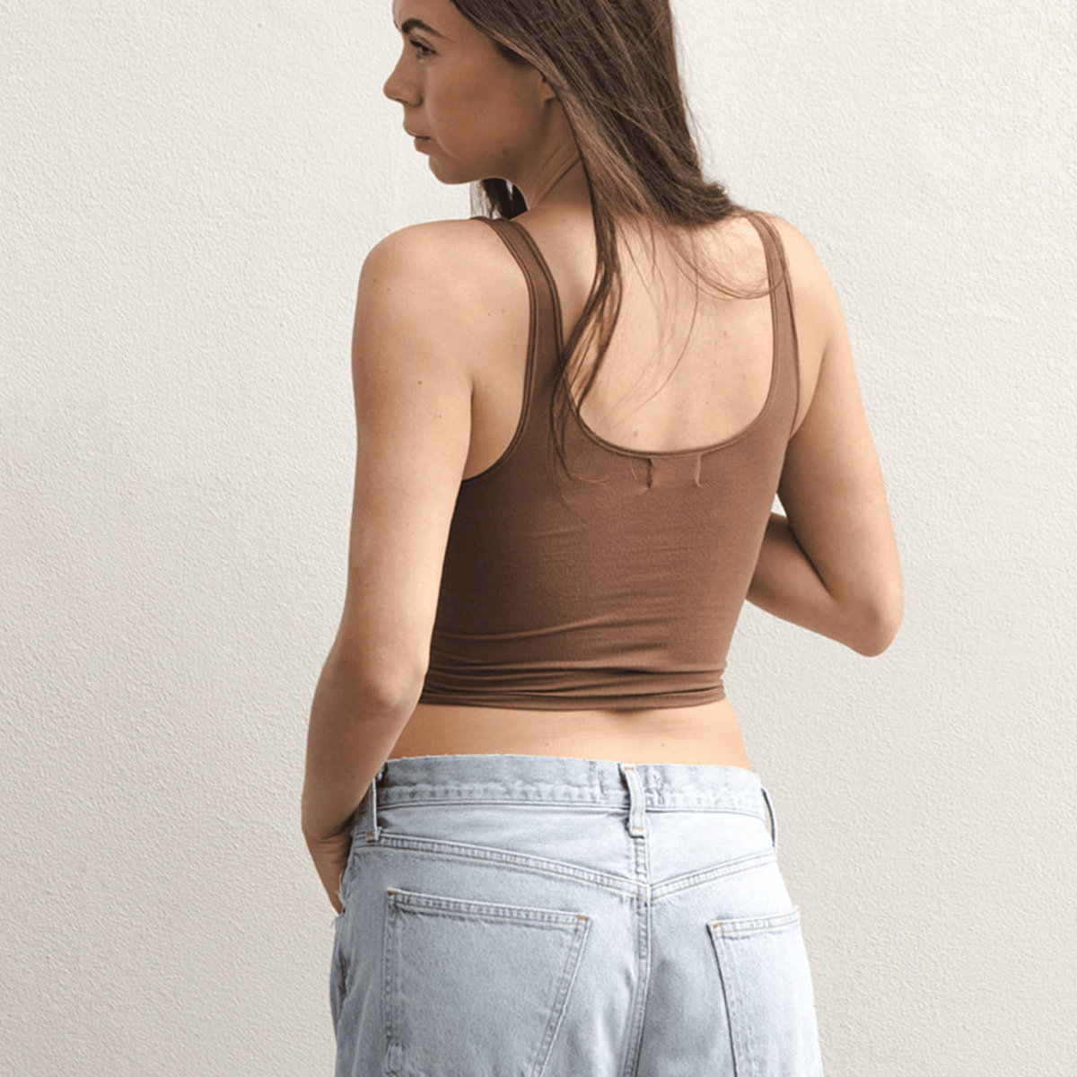 Product shot of NŪD Apparel Devon Double Layered Scoop Crop top, wide strap and seamless, made of bamboo fabric produced in California, in Dark Nude on fair-skinned model paired with light-wash jeans, back shot
