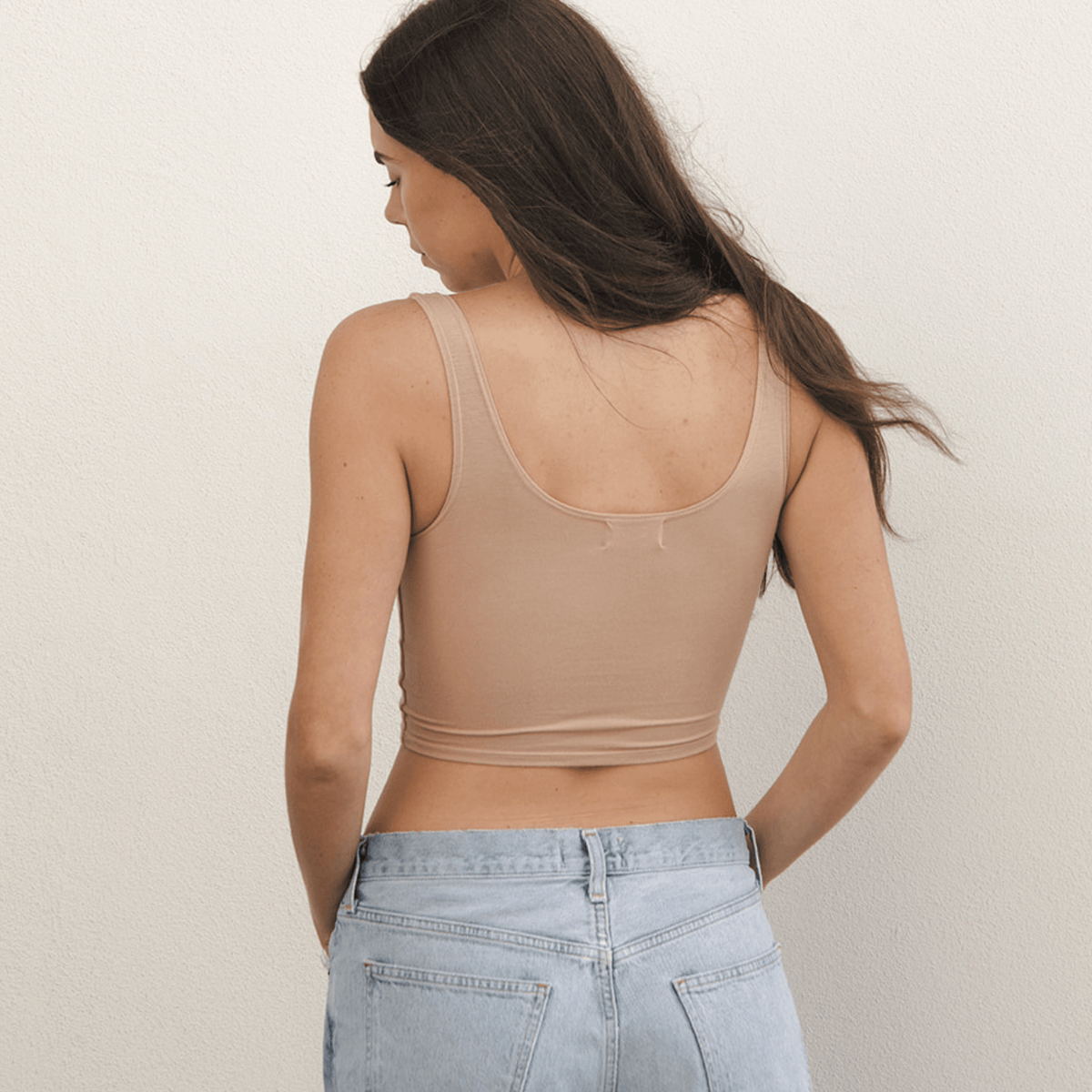Product shot of NŪD Apparel Devon Double Layered Scoop Crop top, wide strap and seamless, made of bamboo fabric produced in California, in Light Nude on fair-skinned model paired with light-wash jeans, back shot