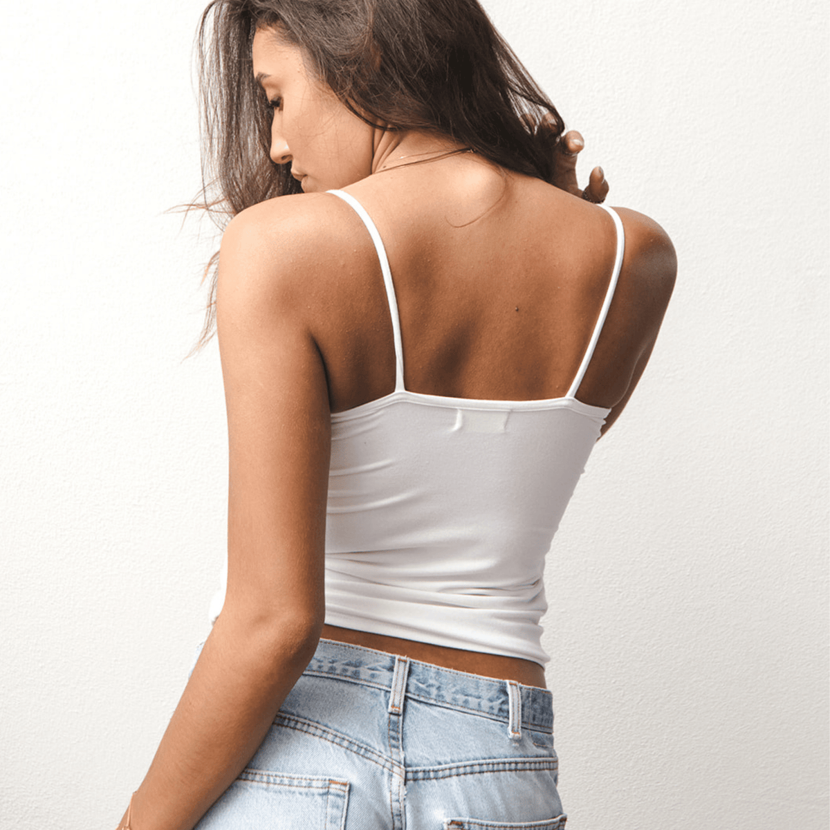 Product shot of NŪD Apparel Nesha Double Layered Tank, thin strap, long style and seamless, made of bamboo fabric produced in California, in White on medium-skinned model paired with light-wash jeans, back shot