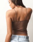 Product shot of NŪD Apparel Nesha Double Layered Tank, thin strap, long style and seamless, made of bamboo fabric produced in California, in Dark Nude on medium-skinned model paired with light-wash jeans, back shot