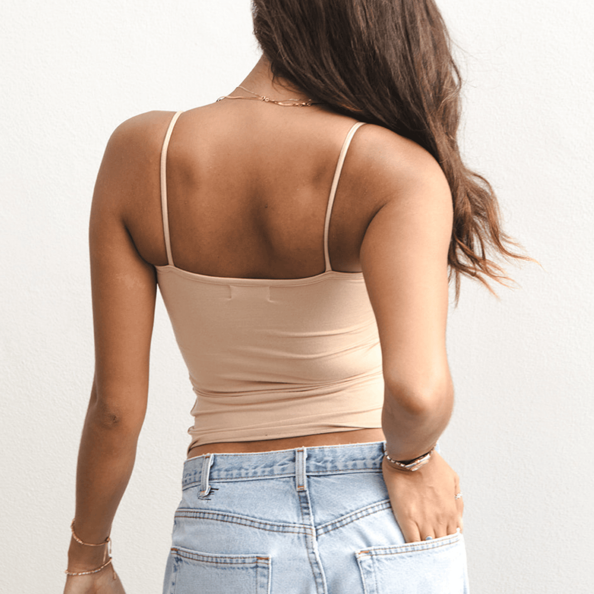 Product shot of NŪD Apparel Nesha Double Layered Tank, thin strap, long style and seamless, made of bamboo fabric produced in California, in Light Nude on medium-skinned model paired with light-wash jeans, back shot