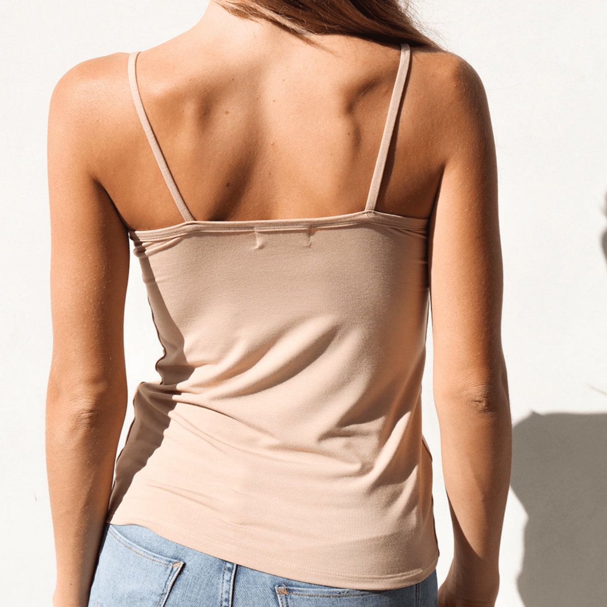 Product shot of NŪD Apparel Nesha Double Layered Tank, thin strap, long style and seamless, made of bamboo fabric produced in California, in Light Nude on fair-skinned model paired with light-wash jeans, back shot