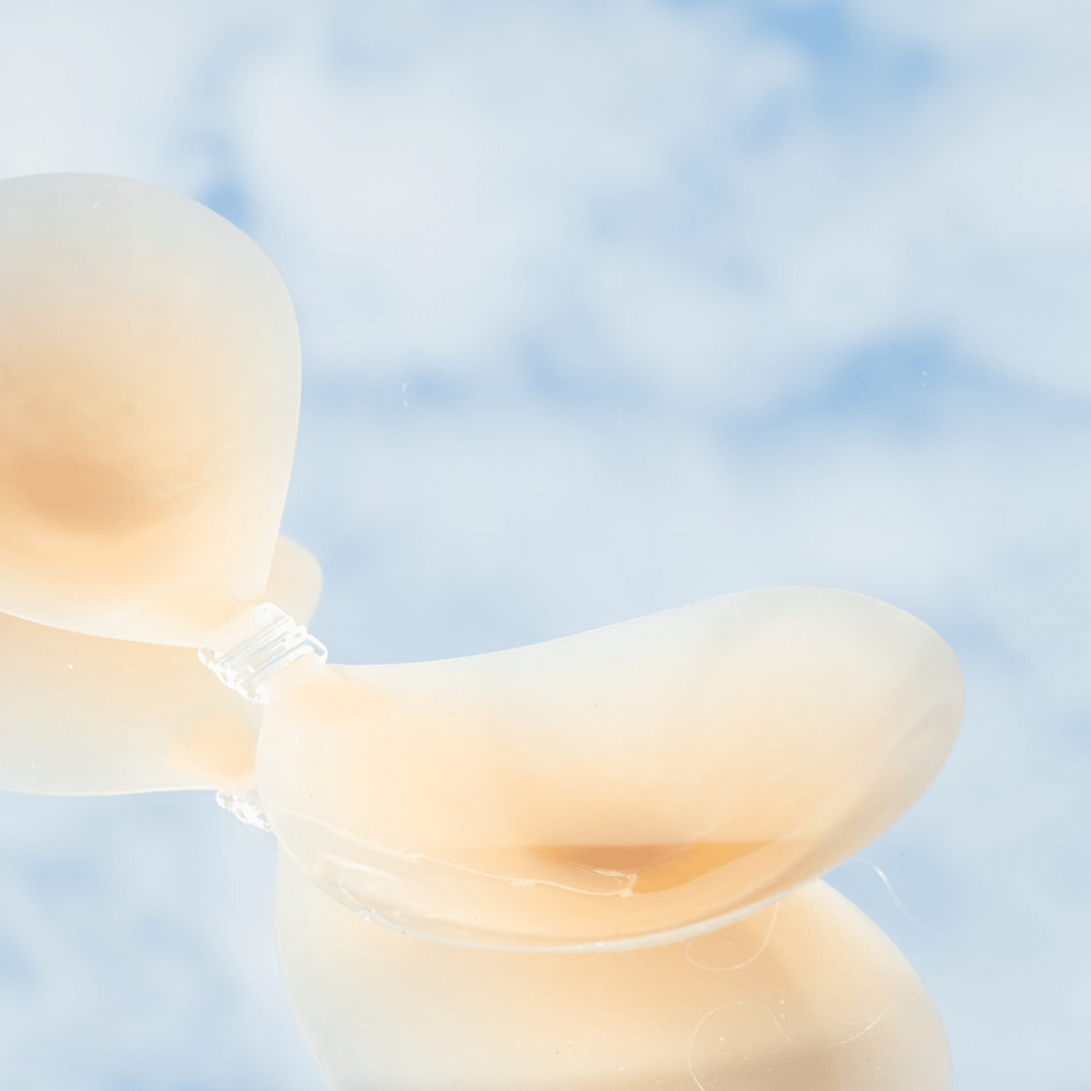 Product shot of reusable and sticky Silicone Stick-on Bra laying flat against mirrored sky background, close-up side shot of the Silicone Stick-on Bra showing the razor thin edges 